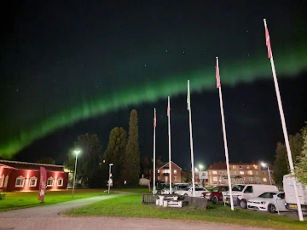 En nattbild av Hotel Nordica, upplyst av säkerhetsbelysning, med en svag norrsken som syns på himlen i bakgrunden.