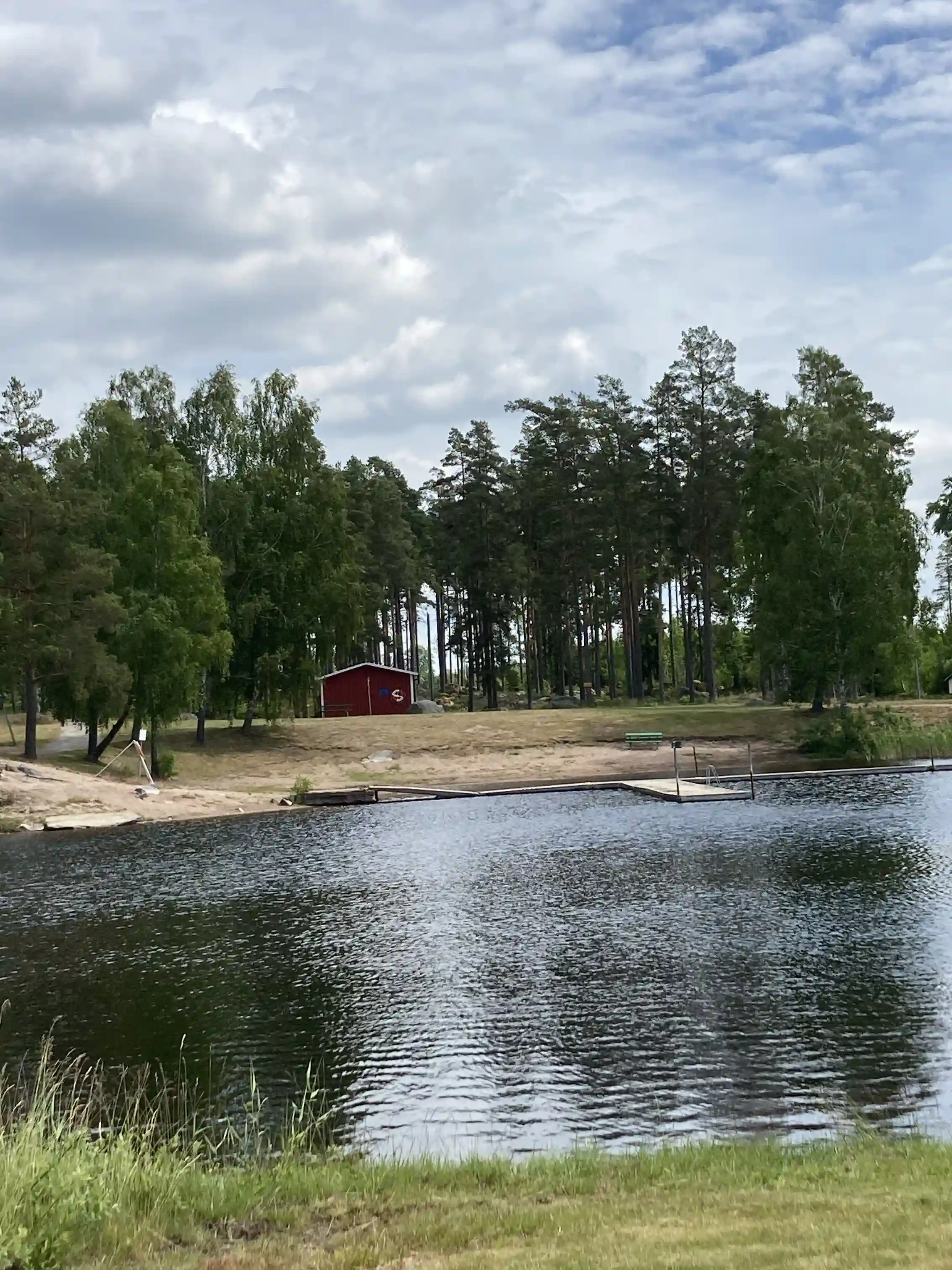 En lugn sjö omgiven av frodig grönska och träd vid Skruvs vildmarkscamping, med vattnet speglande den omgivande naturen och skapar en fridfull atmosfär.