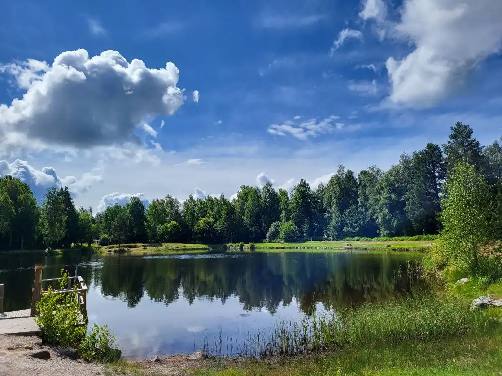 En lugn sjö omgiven av grönskande skog i en vildmarksmiljö vid Skruvs vildmarkscamping.