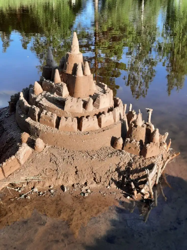 En sandkonstverk i form av ett sandslott vid en strand, omgiven av vildmarksnatur, på Skruvs vildmarkscamping.