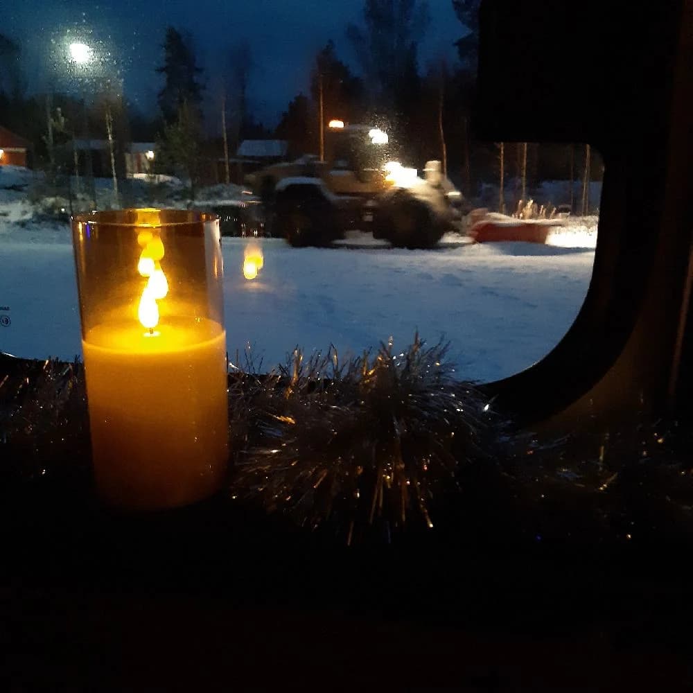 En stämningsfull vinterkväll på Skruvs vildmarkscamping, där ljuset från levande ljus och en öppen eld lyser upp snön i natten.