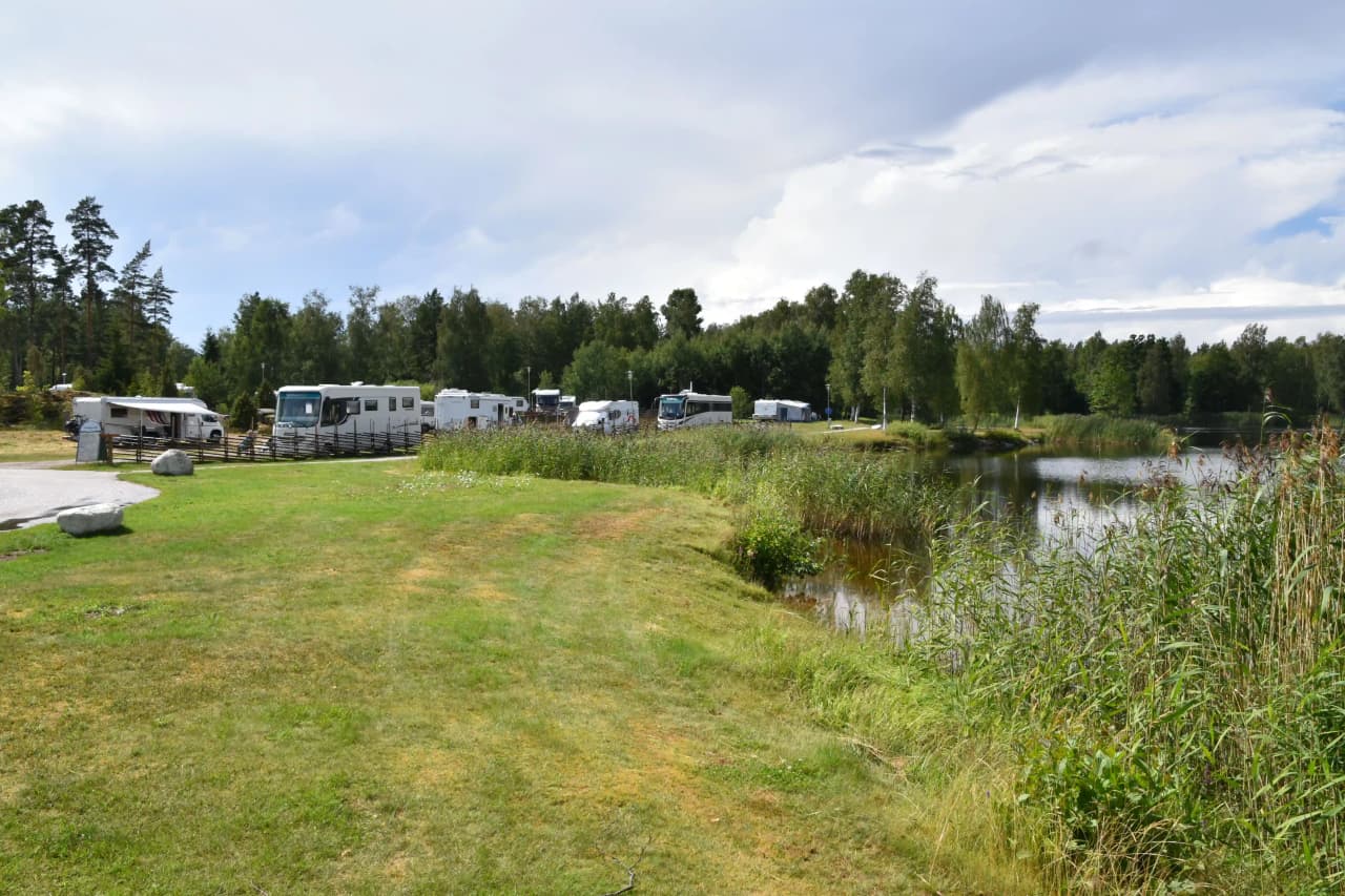 Vy över en rofylld vildmarkscamping vid en stilla sjö omgiven av tät vegetation. Vattenbanor slingrar sig genom landskapet, med kärr och våtmark som skapar en naturlig, orörd miljö.