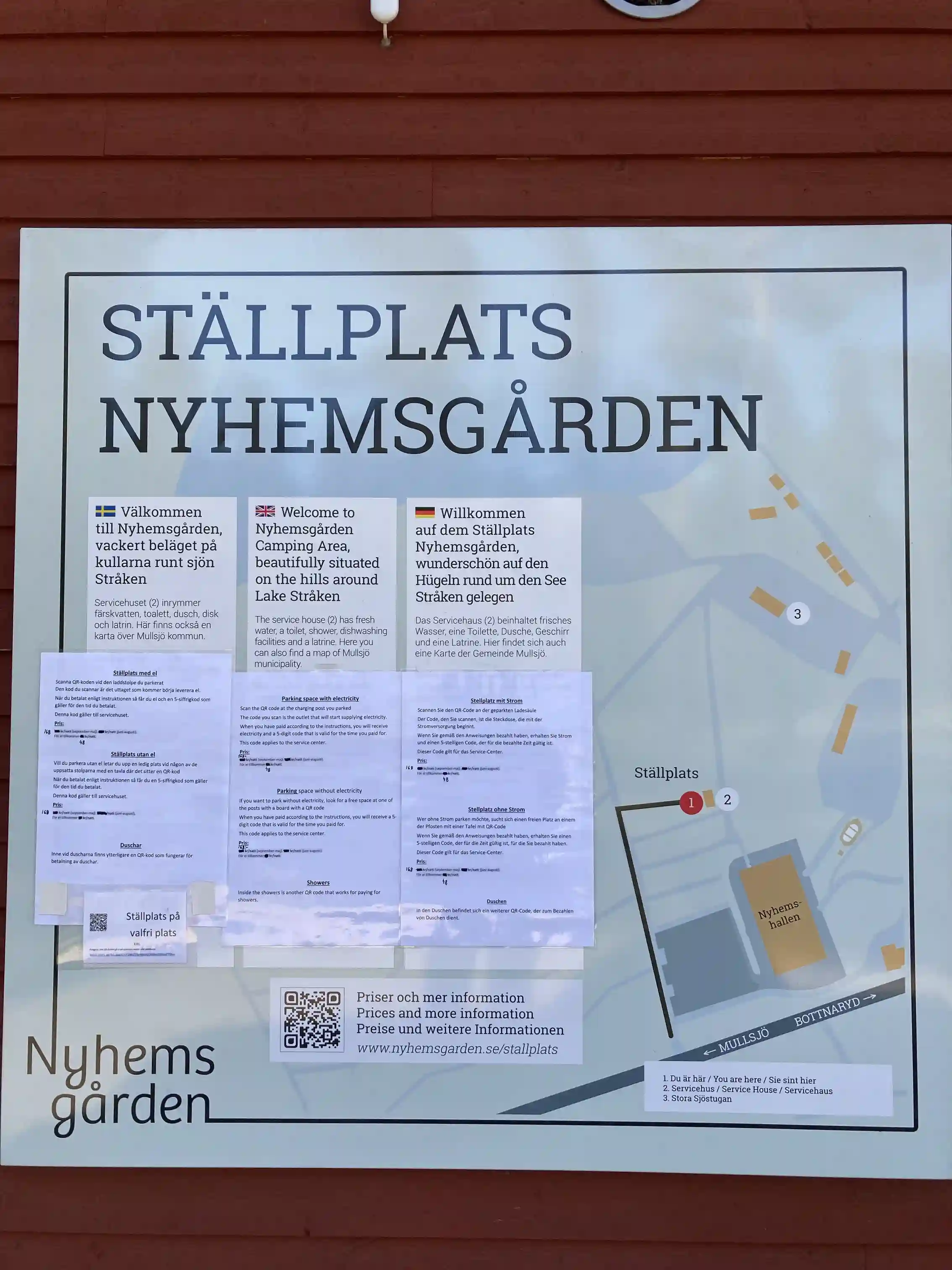 En skylt med texten "Nyhemsgården" i tydlig stil, uppsatt på en byggnad som utgör en del av platsens besöksmål.