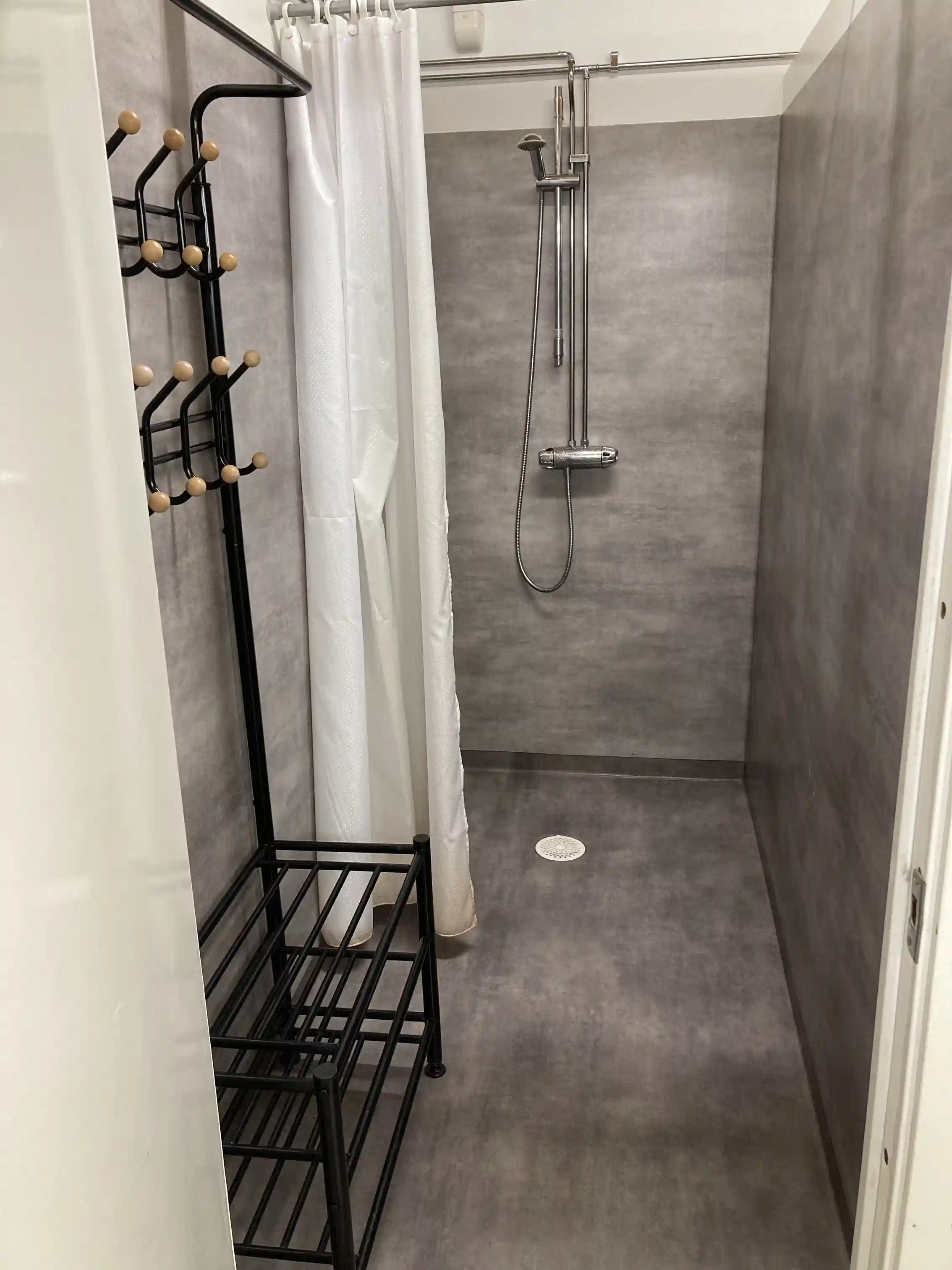 En modern interiör med grått kakelgolv i ett rum, innehållande silverfärgade VVS-armaturer och badrumsinredning.