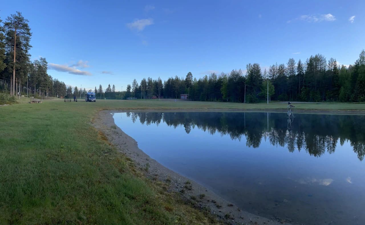 En lugn sjö vid Ljusvattnets camping med klarblått vatten och omgivande träd som speglas på ytan.