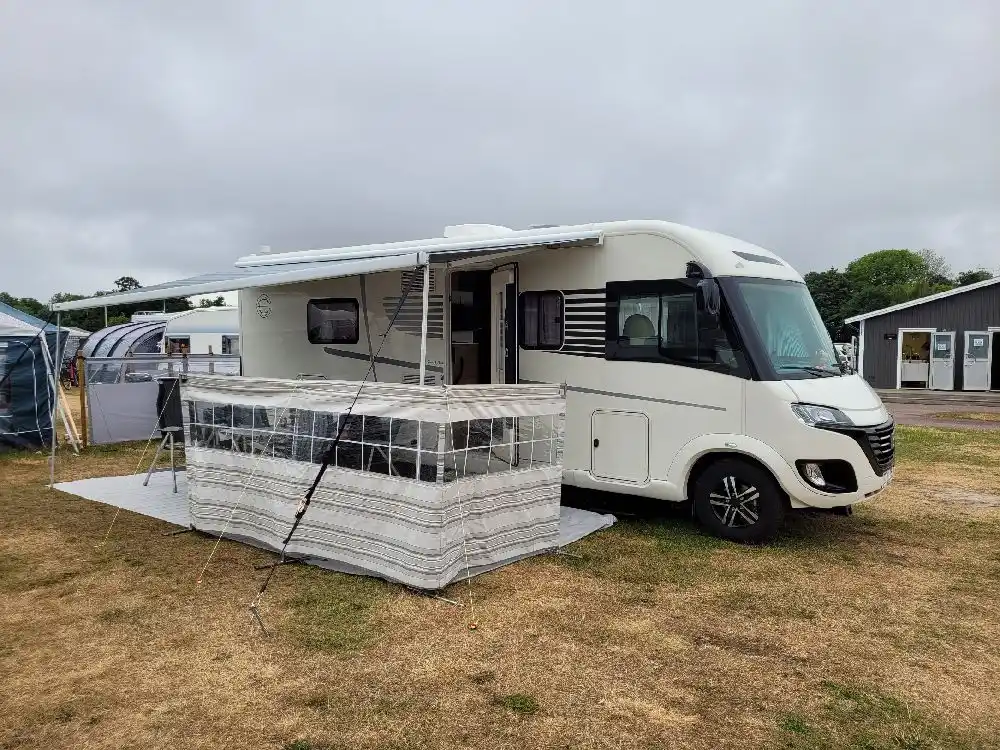 Bild av Sandbybadets camping som visar flera husvagnar och husbilar parkerade på campingplatsen. Området är fyllt med fordon av olika typer, inklusive husvagnar och mobila hem, som står uppställda på rad. Umgebung är trädbevuxen med vägar mellan campingplatserna.