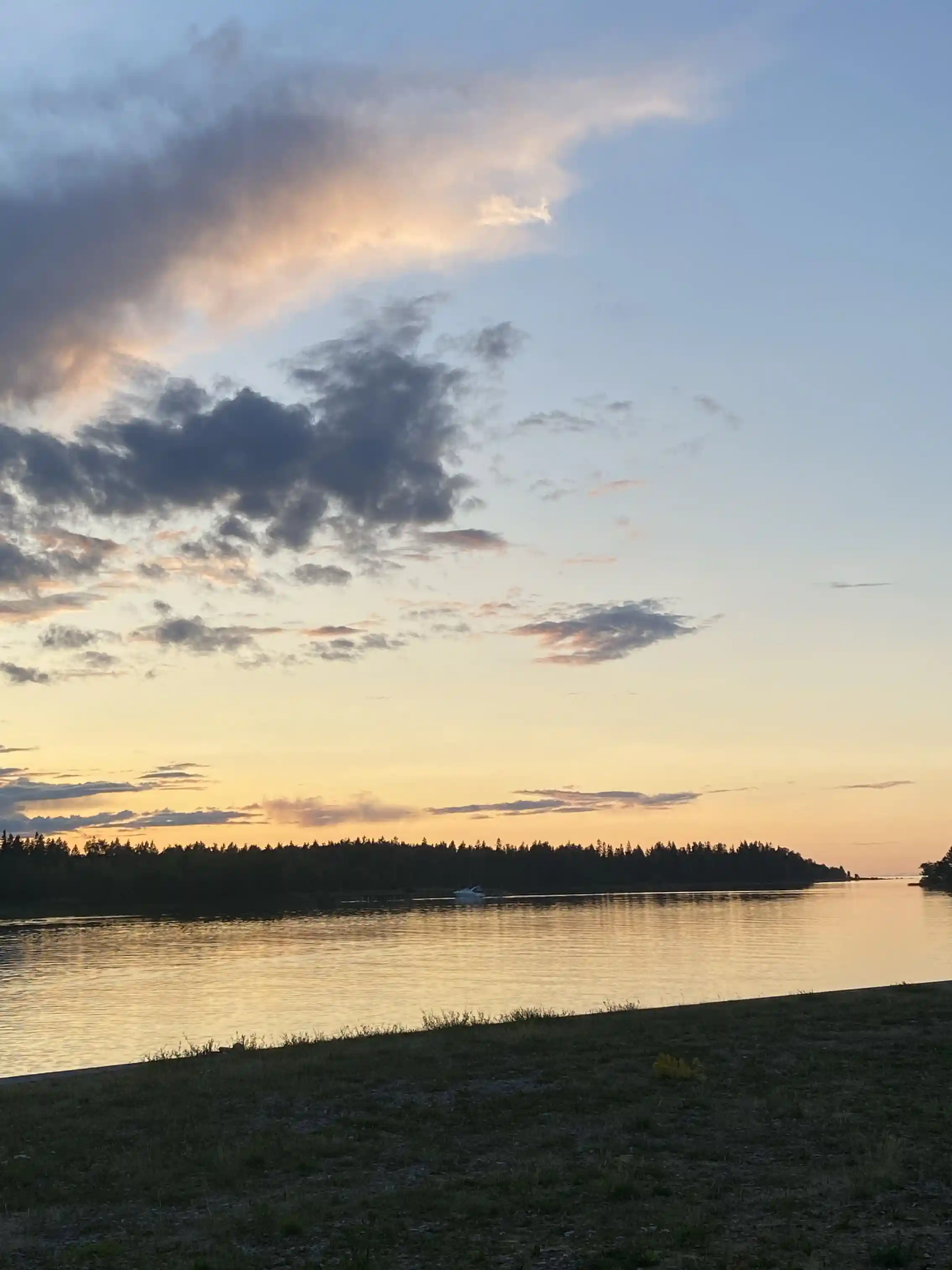 En vy av Hargshamns camping vid vattnet under en klarblå himmel med några moln i horisonten, skymningen börjar lägga sig vilket ger en varm efterglöd över landskapet.