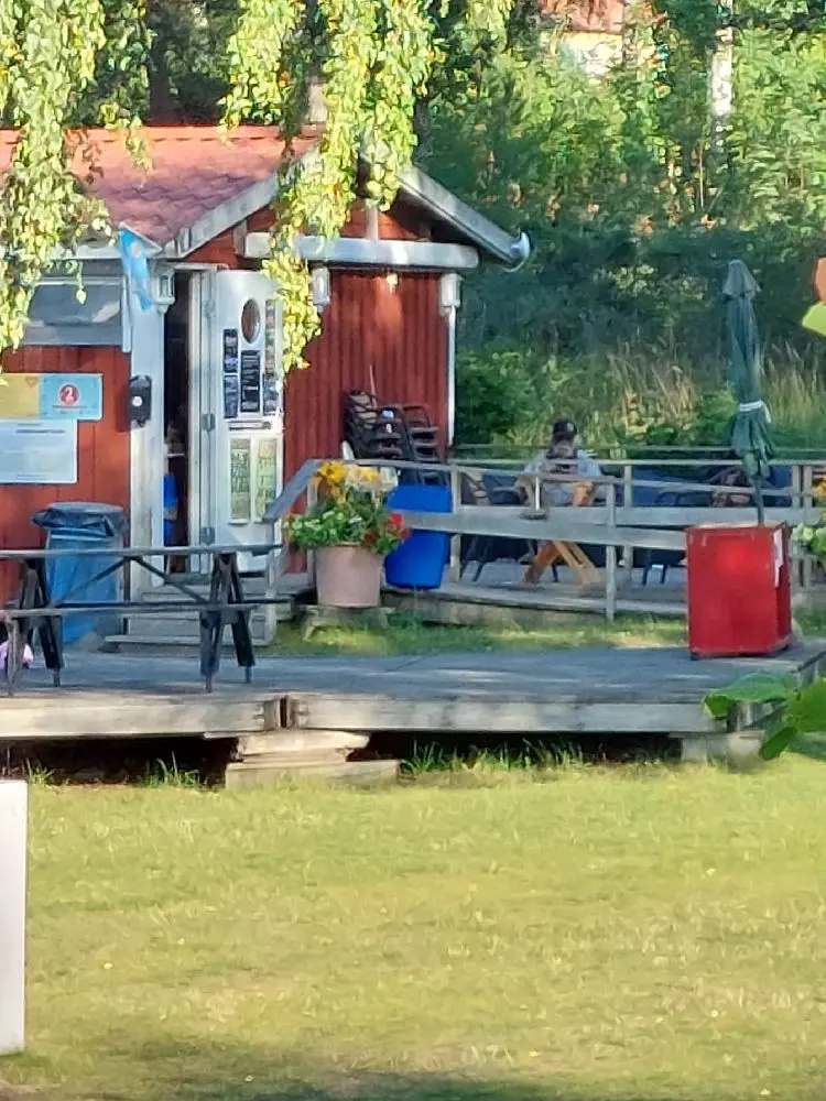 En campingplats med utomhusmöbler som inkluderar bord, stolar och en bänk under skugga, omgiven av grönska i en avslappnad miljö på Hargshamns camping.