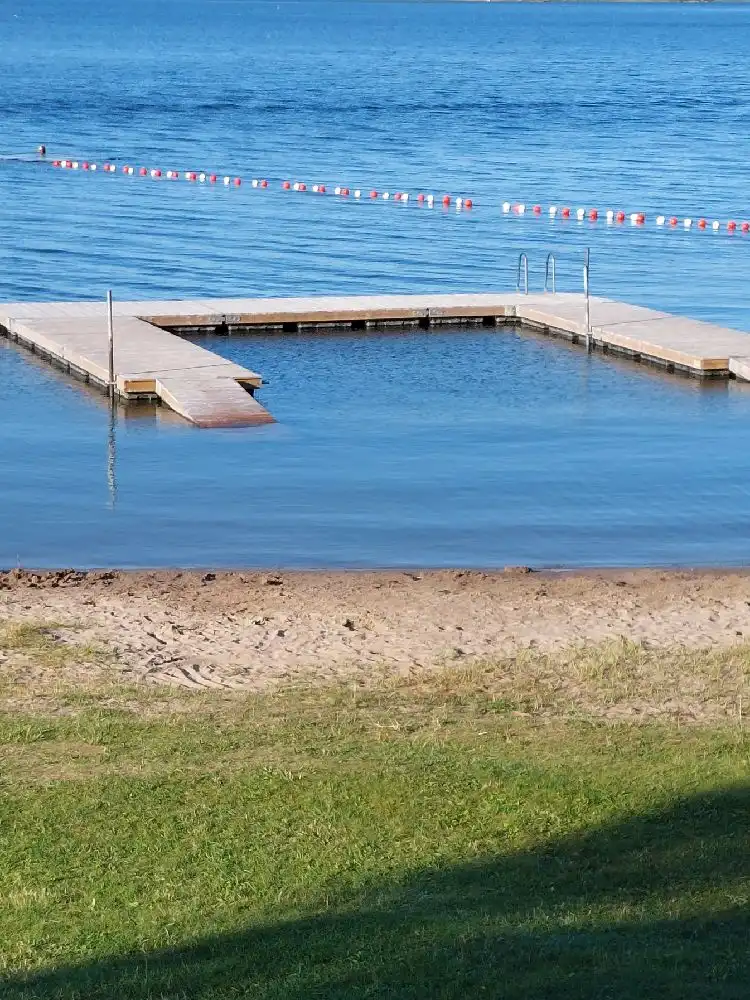 En brygga som sträcker sig ut i en sjö vid Hargshamns camping, omgiven av lugnt vatten och grönskande omgivning.