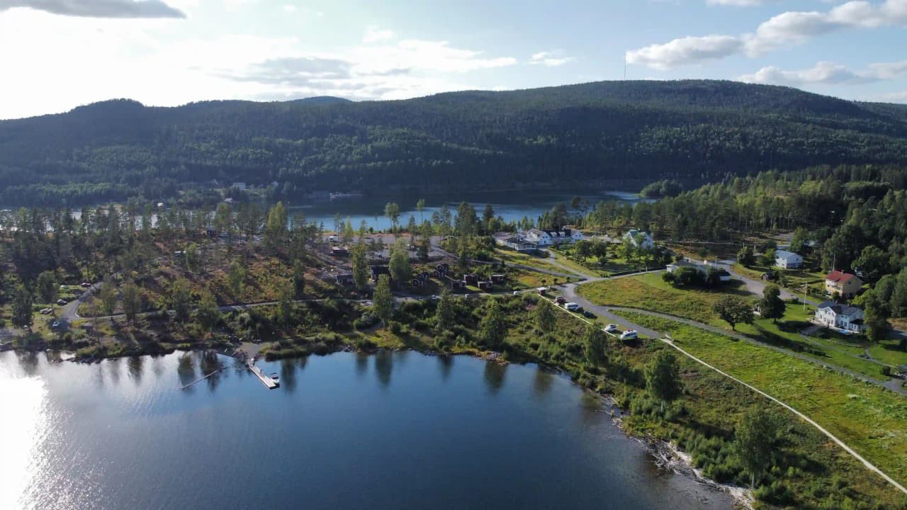 En naturskön vy av Måvikens camping & naturområde, med en stor vattenresurs omgiven av böljande landskap och frodig natur.