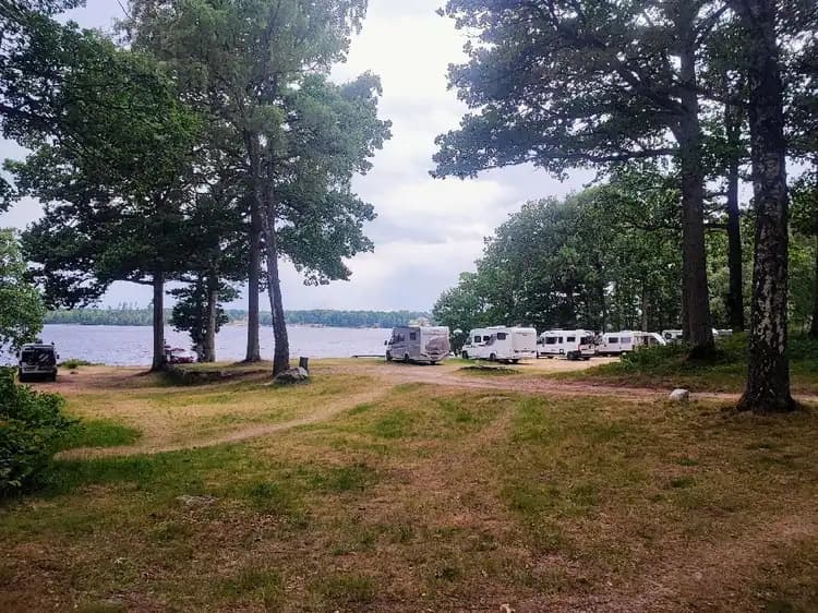 En naturskön kustlinje med en glittrande sjö omgiven av grönska. En sandstrand löper längs vattnets kant med träd och buskar i bakgrunden, vilket skapar en fridfull och inbjudande atmosfär på Hägern Bed & Nature.