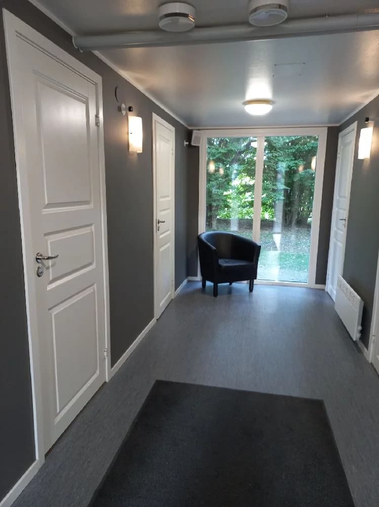 En interiörbild från en byggnad vid Gålö Havsbad, med trägolv och träpaneler på väggar och tak. En dörr syns i rummet, som förmedlar en hemtrevlig atmosfär.