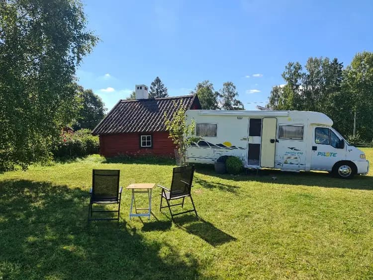 En parkerad husvagn på en grön gräsmatta vid Kvarngården hembygdsgård. I bakgrunden syns en annan större husvagn, samt träd och en öppen yta.