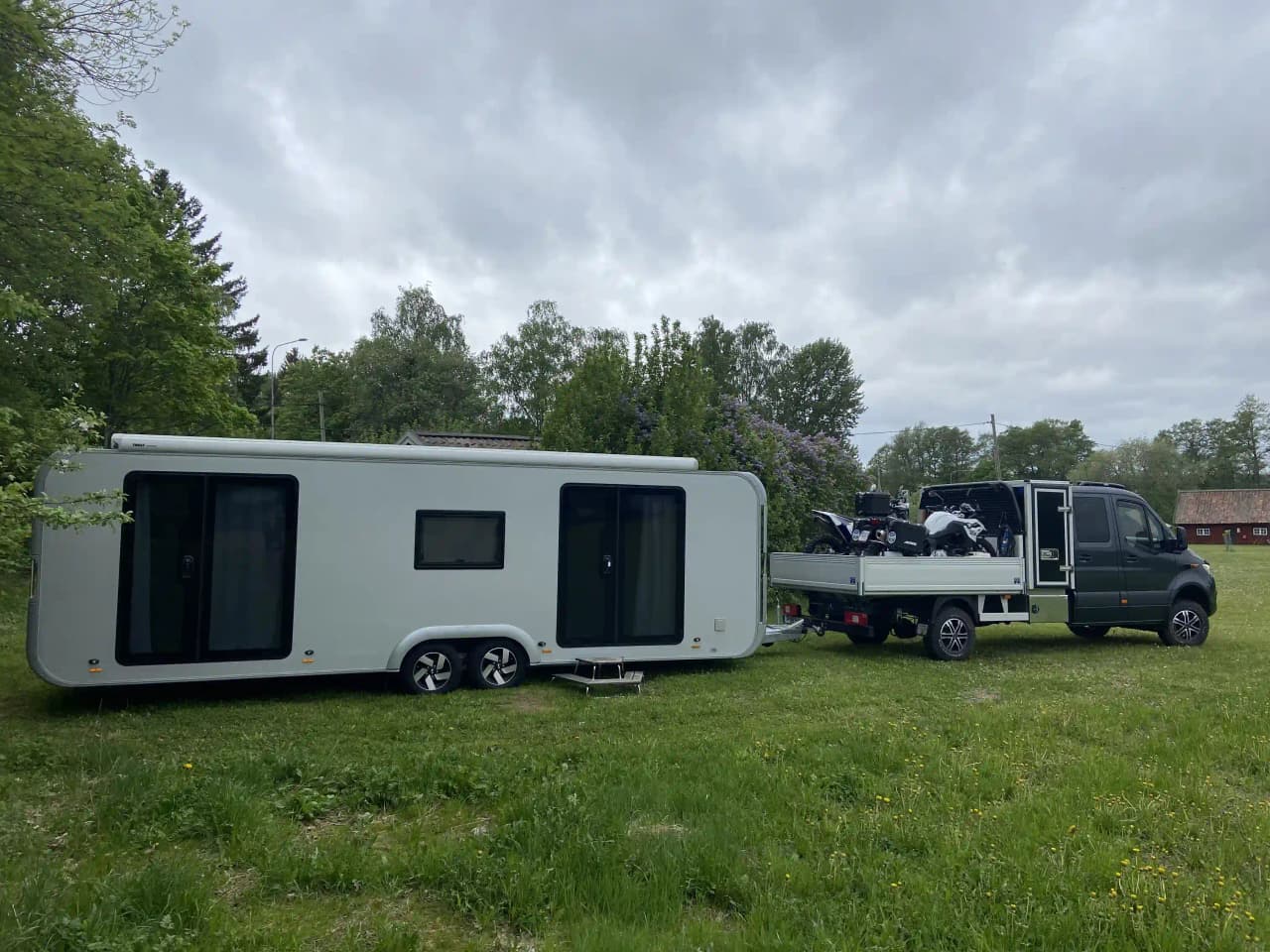 Bild av en parkerad husbil vid Kvarngården Hembygdsgård, omgiven av gröna träd och en traditionell byggnad i bakgrunden.