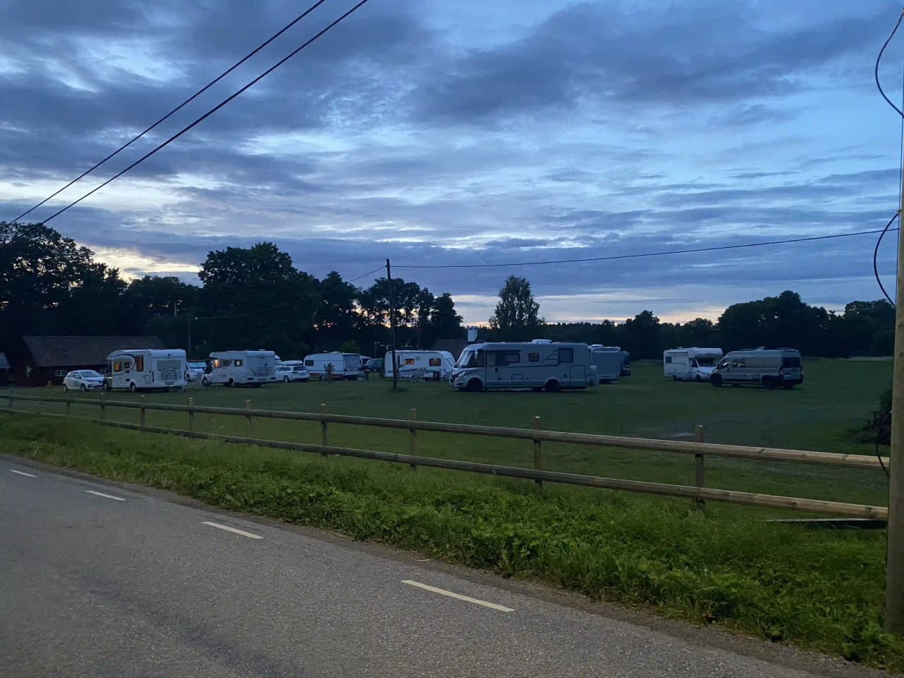 En husbil och en skåpbil är parkerade på en gräsmatta under en molnig himmel vid kvarngården hembygdsgård.