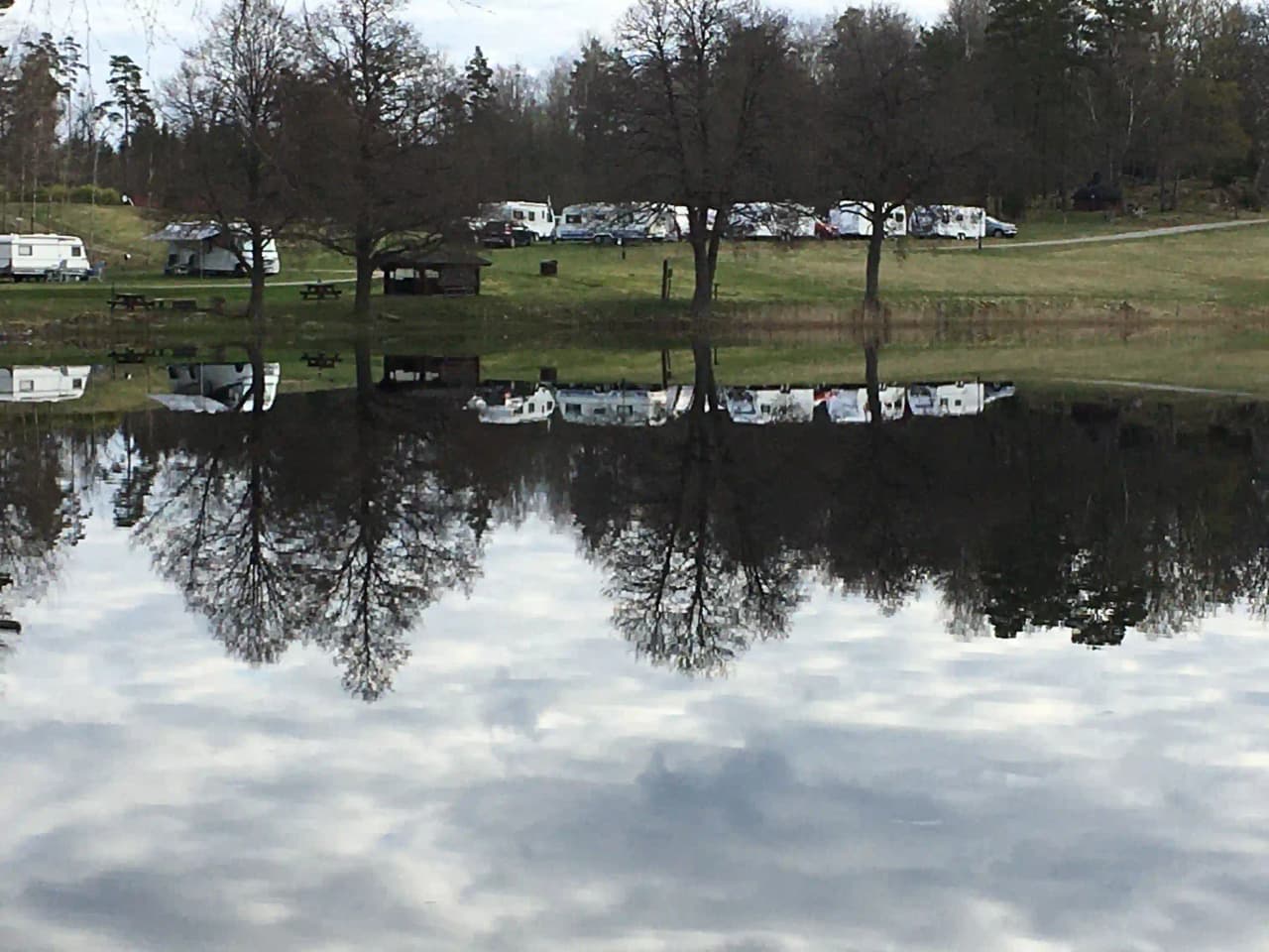 En lugn vattenväg som speglas av den omgivande naturliga miljön vid Påarps gård, med grönska längs strandkanten under en klar himmel.