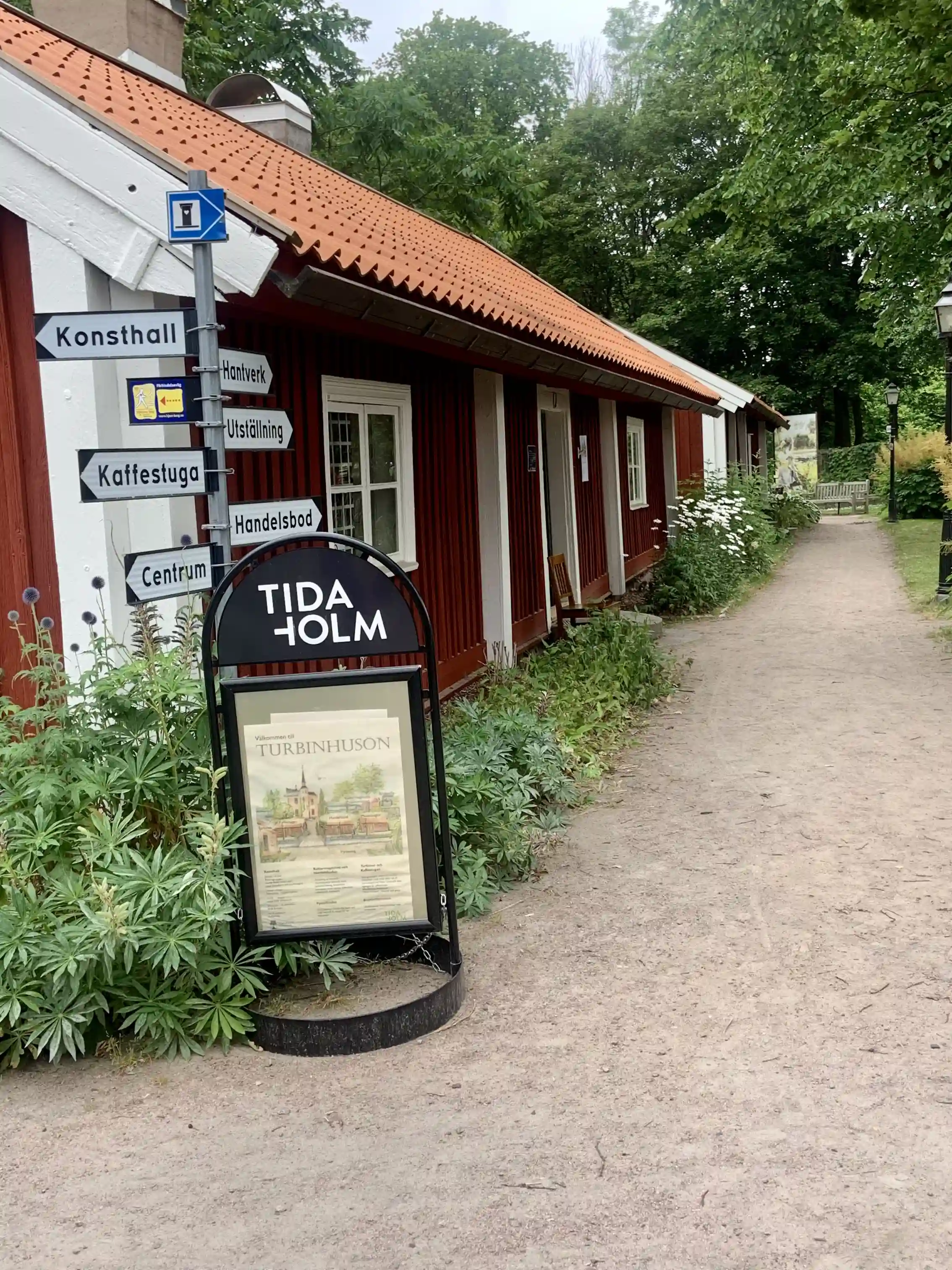 En naturskön campingplats med grönska och en fridfull atmosfär, där besökare kan se ett värdshus med tillhörande campingfaciliteter i bakgrunden.