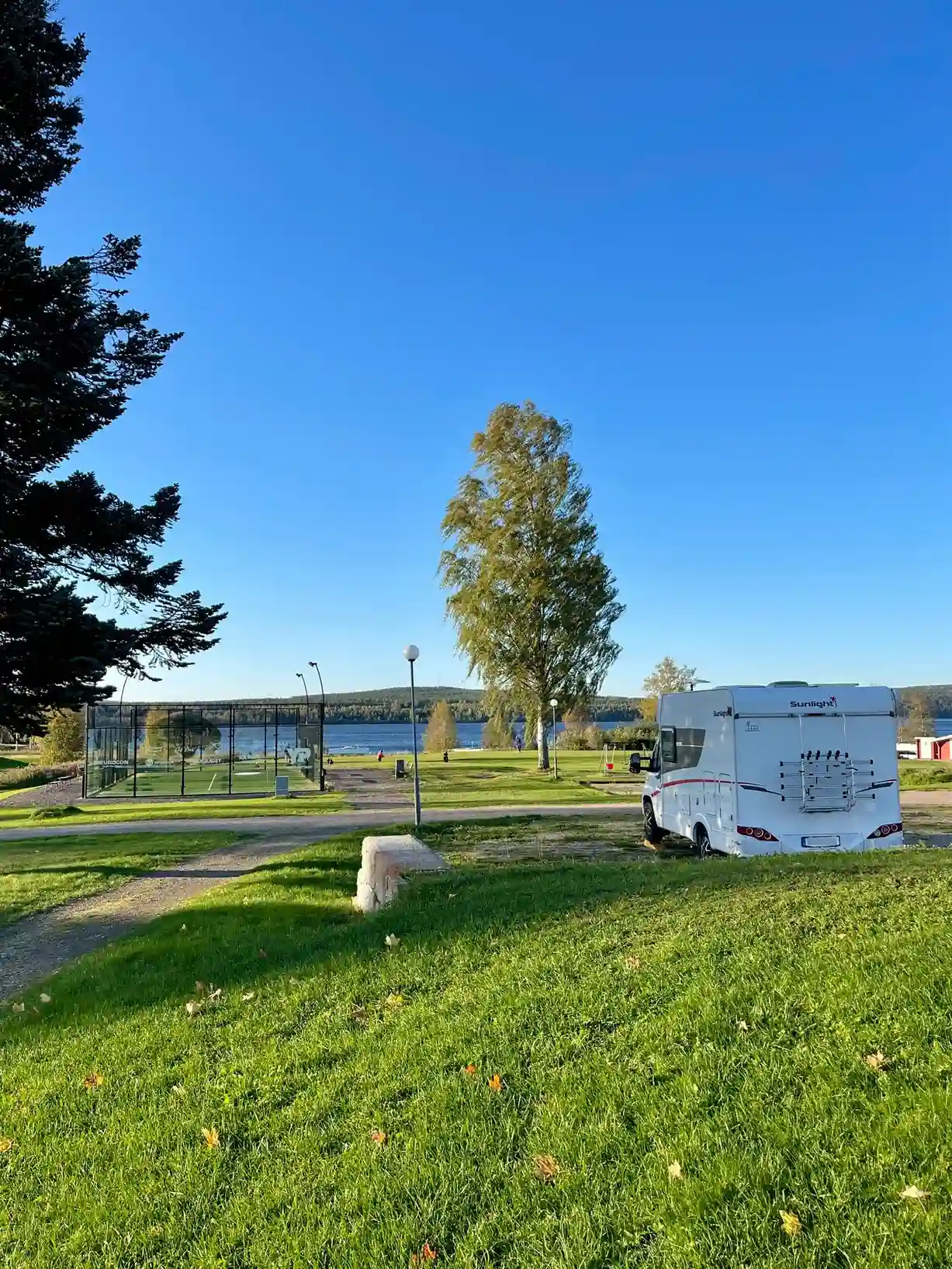 En grön gräsyta på Öjestrand GK, med husvagnar i bakgrunden och höga stolpar som ger skugga.