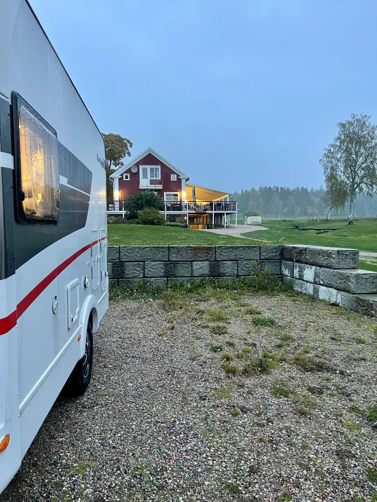 En husvagn står parkerad på en gräsmatta vid Öjestrand GK, med en välskött trädgård och parkmiljö i bakgrunden.