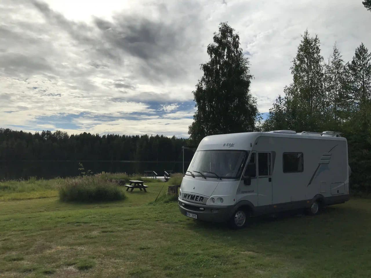 En bild av en husvagn och två andra fritidsfordon på Rossön camping, omgivna av grönska och träd.