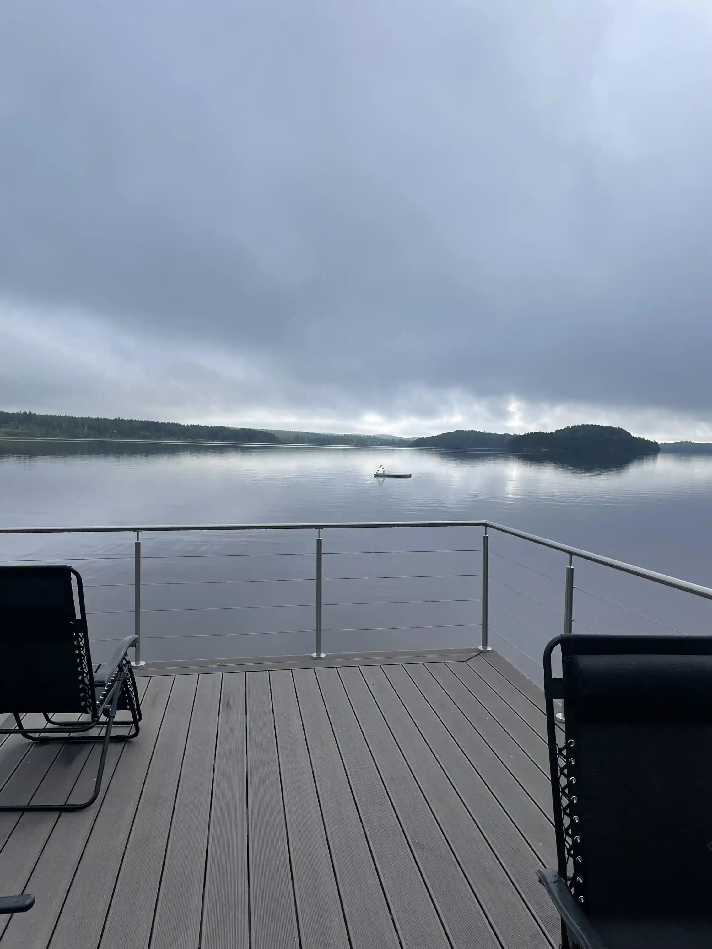 Alt-text: En träbrygga med räcke vid en sjö, där det grå träet kontrasterar mot det blå vattnet.