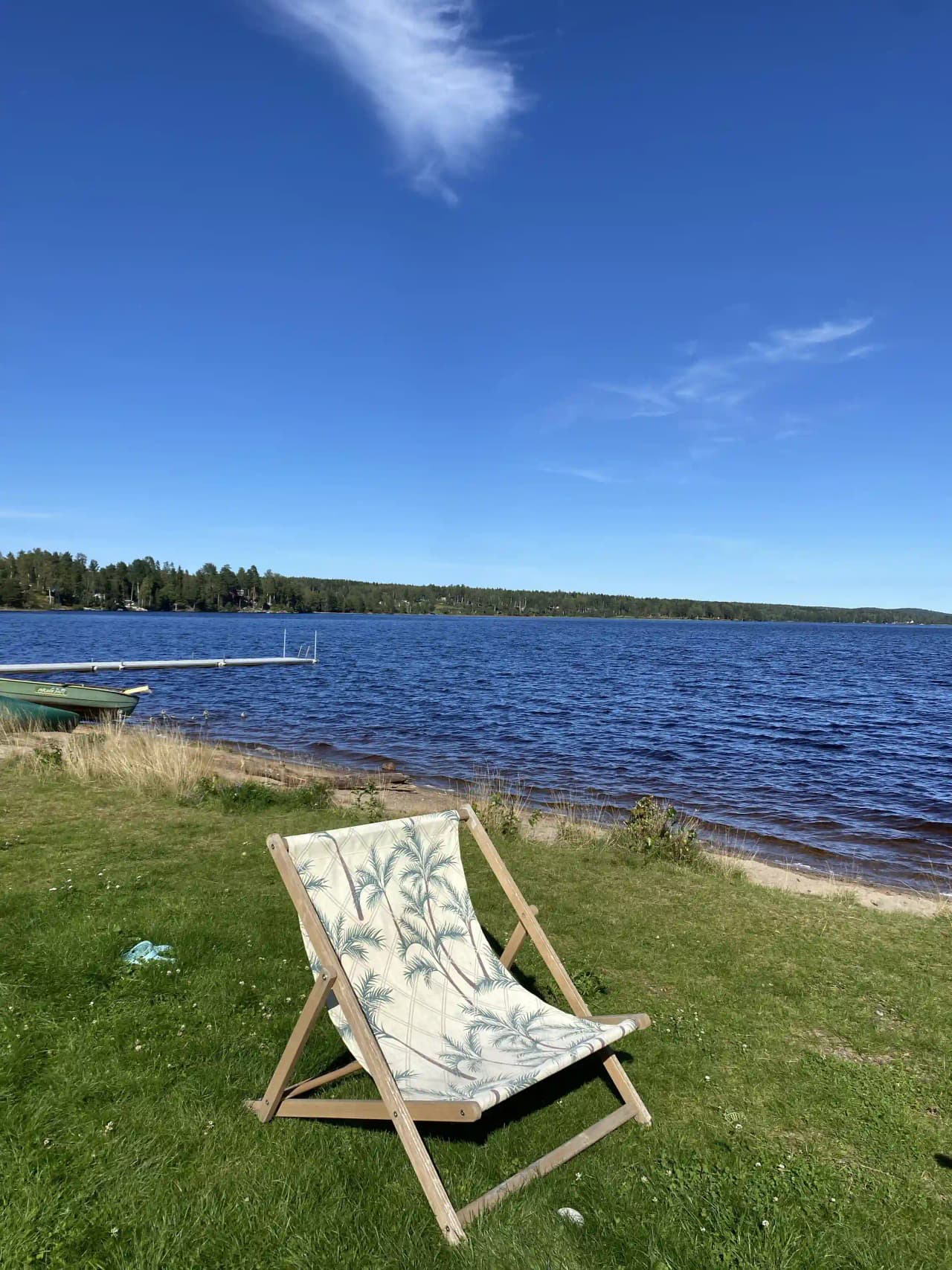En blå hopfällbar stol står på en kustnära plats vid havet, belyst av solljus med en vy över stranden och vattnet i bakgrunden.