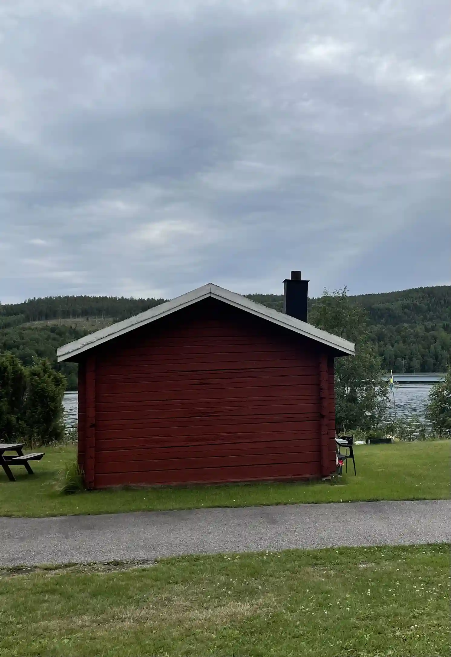 En grön campingplats med gräs och små stugor, belägen vid en vacker sjö, omgiven av natur och lugna omgivningar.