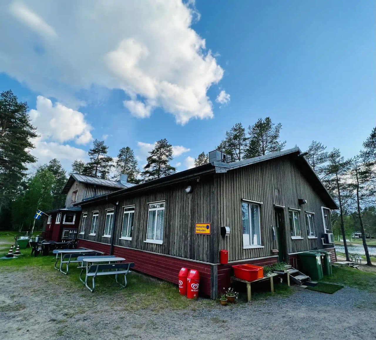 En mysig timmerstuga omgiven av grönskande träd med en picknickbord och bänkar i trädgården, idealisk för utomhusaktiviteter och avkoppling.