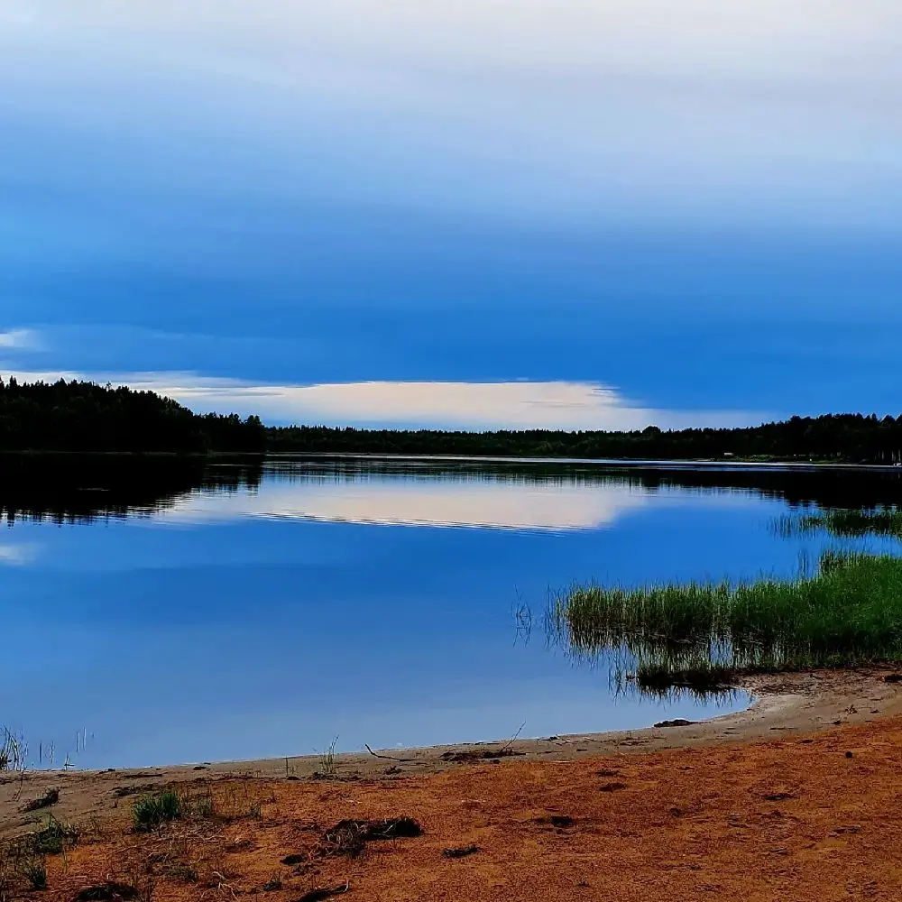 En bred vy över en klar blå himmel och ett stilla vattendrag, där horisonten möter ett naturlandskap med vita moln i bakgrunden, vilket framhäver Vallens turism och fritids natursköna omgivningar.