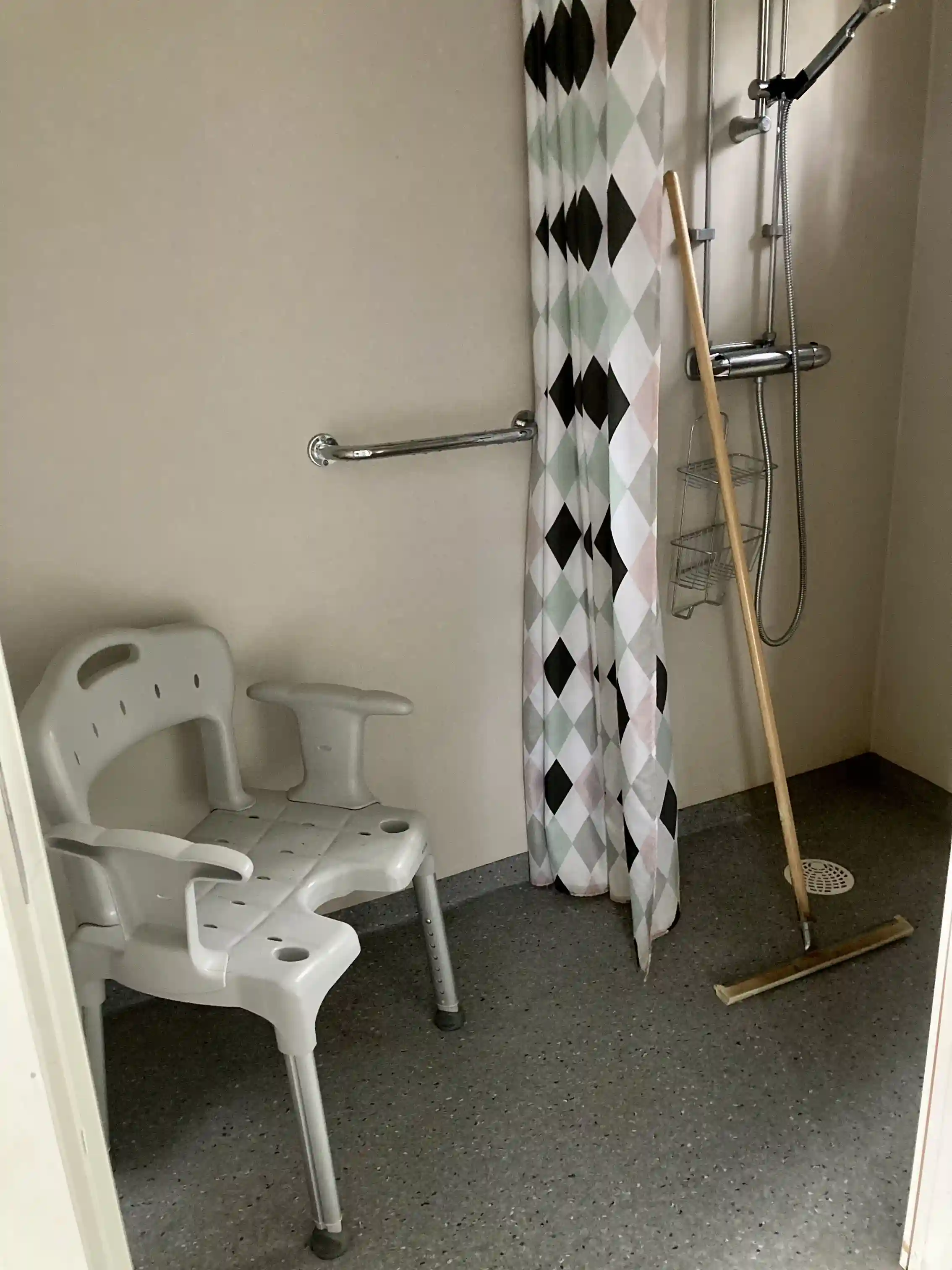 Ett badrum med kaklat golv och väggar, silverfärgade VVS-armaturer och ett modernt handfat. Rummet framstår som rent och välhållet.