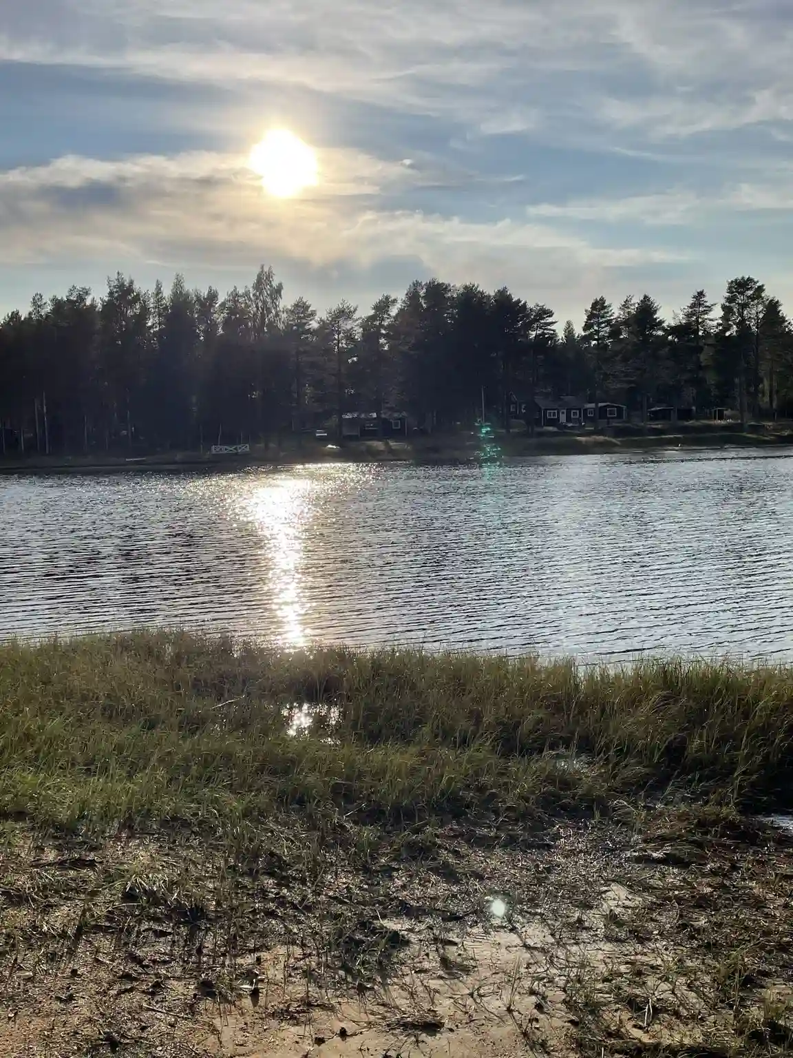 En rofylld sjö med en vid horisont under en molnig himmel. Vattnet speglar den lugna naturen omkring, medan en strandlinje kantar sjöns kust.