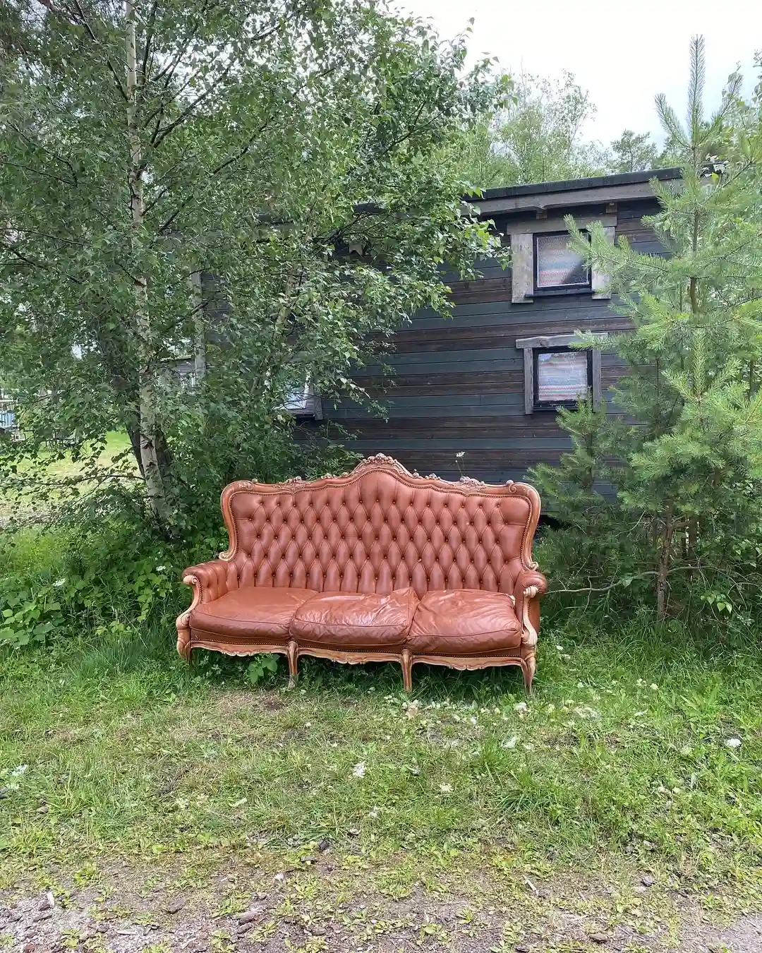 En utomhusmiljö vid Fide Äventyrsby & Camping med bekväma trämöbler, inklusive en dagbädd, en soffa och en bänk, placerade på en gräsmatta i solen.