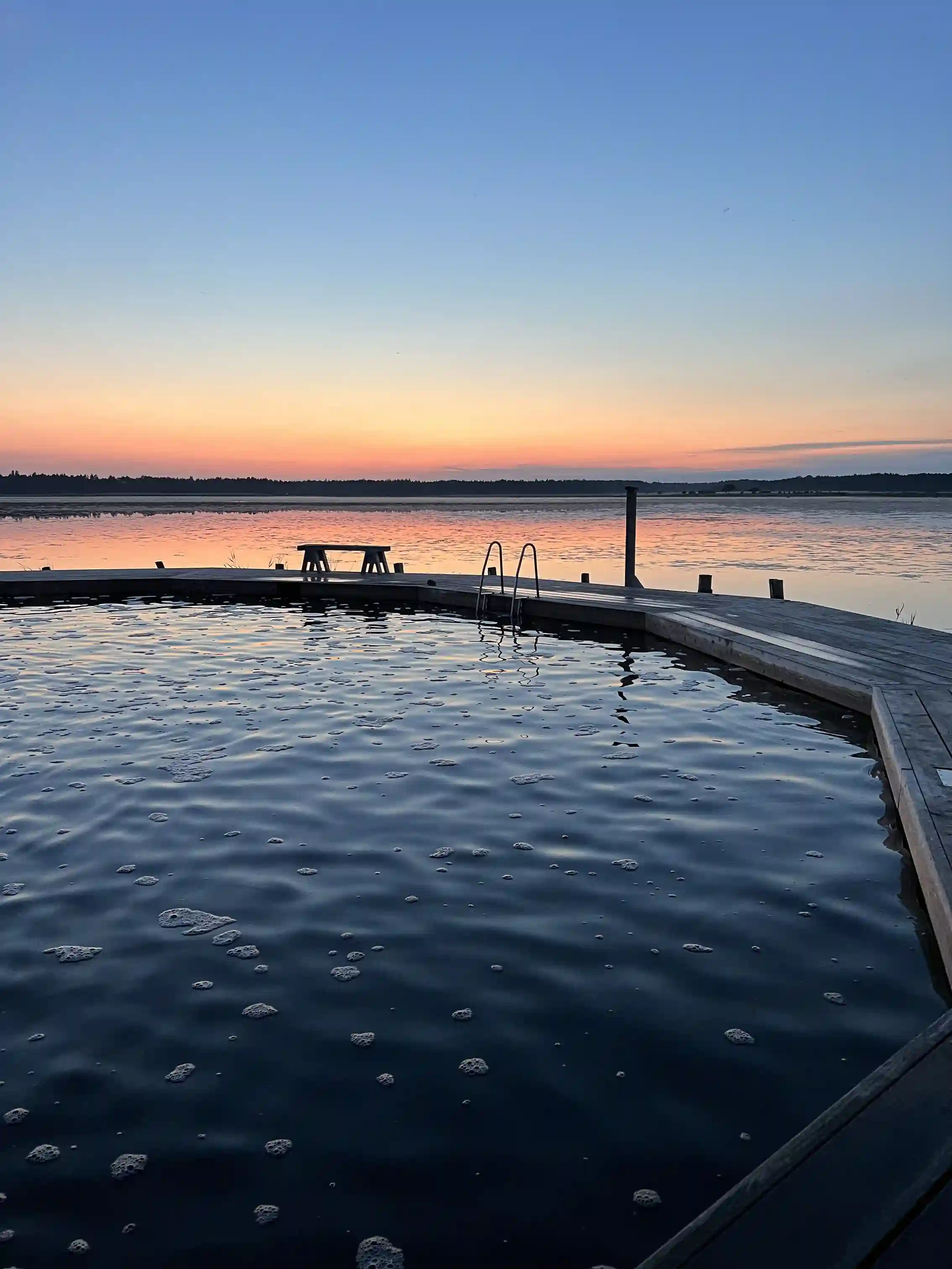 En lugn sjö vid solnedgången med ett blått vatten och en vidsträckt horisont i bakgrunden.