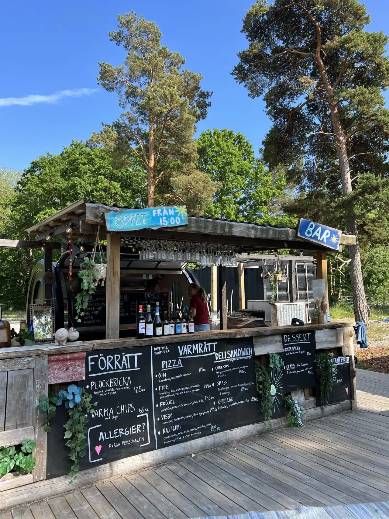 En utomhusmiljö på Fide Äventyrsby & Camping med picknickbord och bänkar under skuggande tak, redo för besökare att njuta av en paus i det offentliga området.