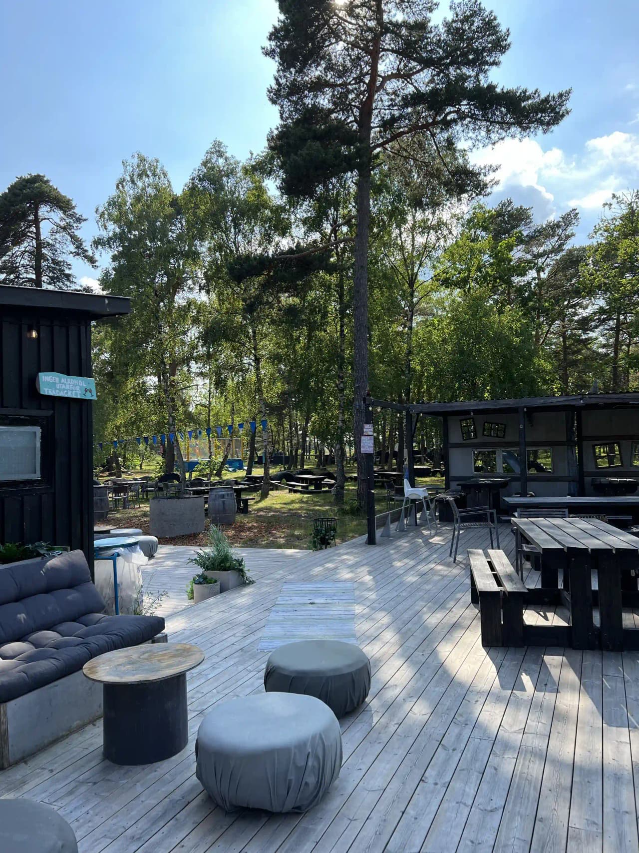 En uteplats med picknickbord och bänkar under ett skuggande tak, omgiven av gröna områden i Fide Äventyrsby & Camping.