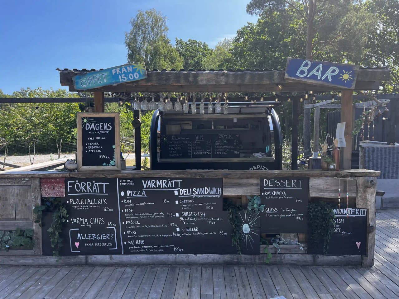 En skuggig uteplats vid Fide Äventyrsby & Camping med träbord, bänkar och plankor, idealisk för avkoppling och utomhusmåltider.