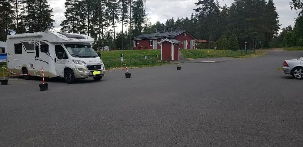 En husbil parkerad på en asfalterad uppfart vid Hjortsjöns camping, omgiven av andra fordon och grönska.