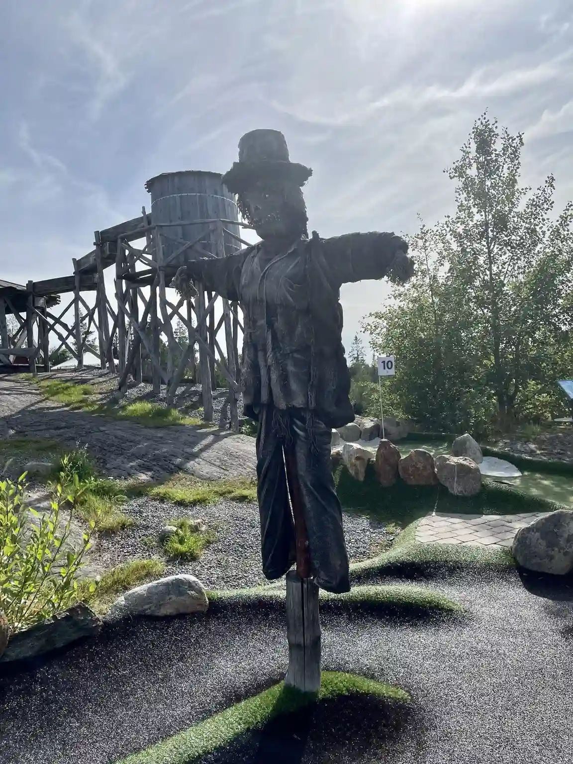 En konstnärlig skulptur eller staty, liknande en fågelskrämma, står på gräsmattan vid Lufta Camping & Restaurang, inramad av omgivande natur.