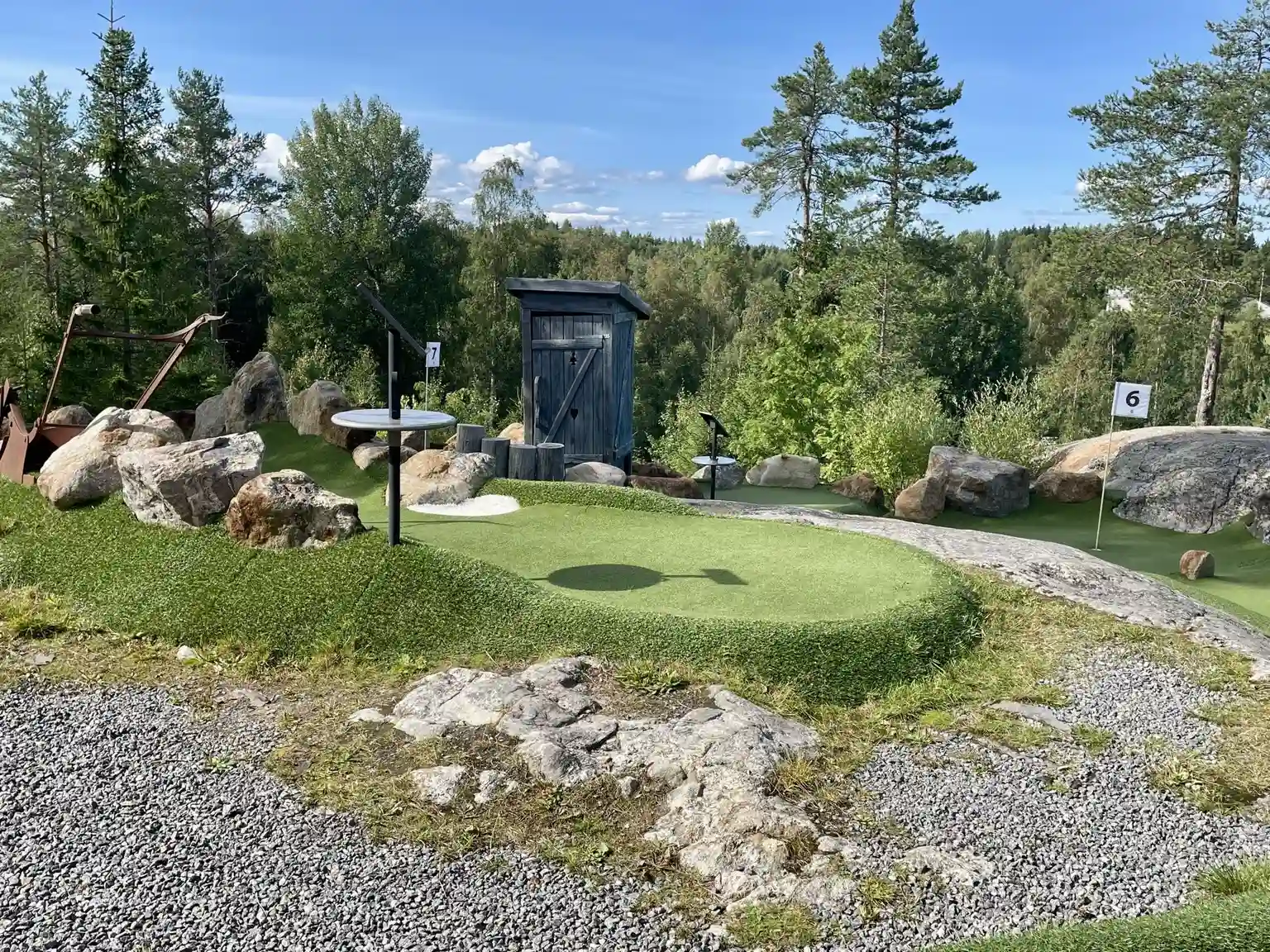 En grönskande campingplats med välskötta trädgårdar och stenlandskap, inklusive stora stenblock och frodiga gräsmattor. Området liknar en botanisk trädgård med harmonisk parkmiljö, perfekt för avkoppling och rekreation.