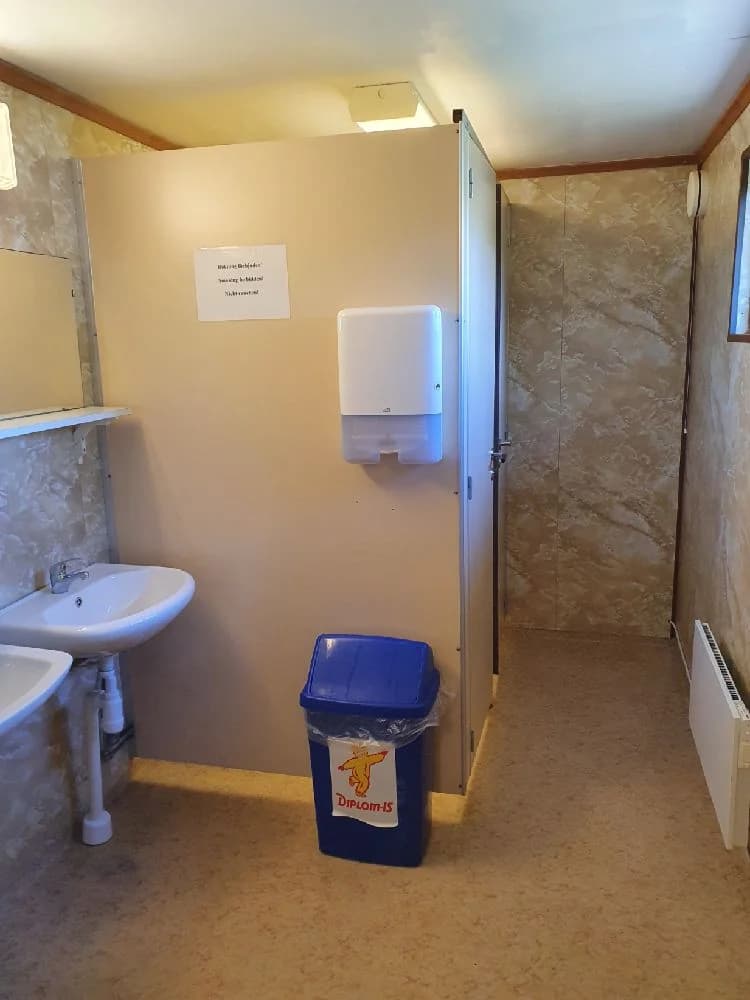 En välstädad campingtoalett med trägolv, kaklade väggar och ett modernt tvättställ. Ljusa trädetaljer och en ren, praktisk design skapar en inbjudande atmosfär.