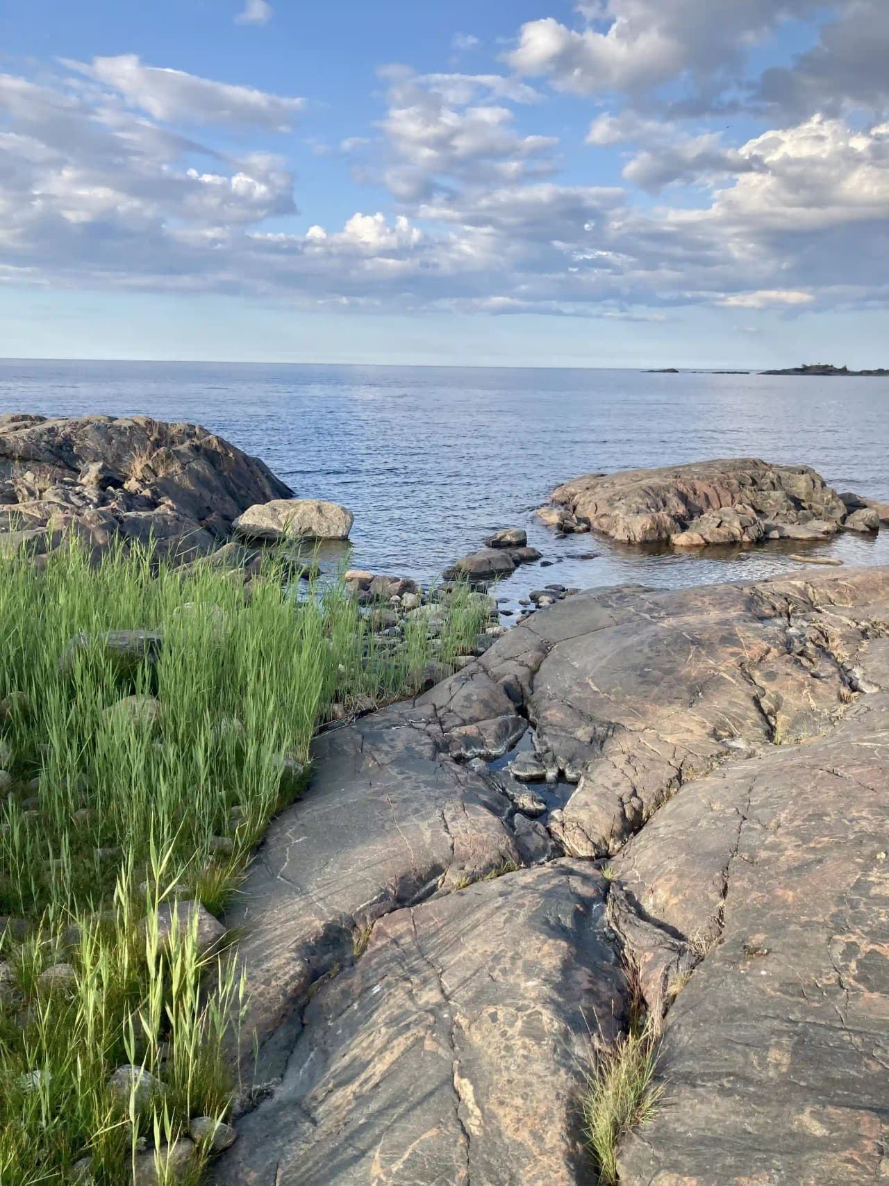 En kustlinje med klippor och havsvatten under en blå himmel vid Ängskärs havscamping.