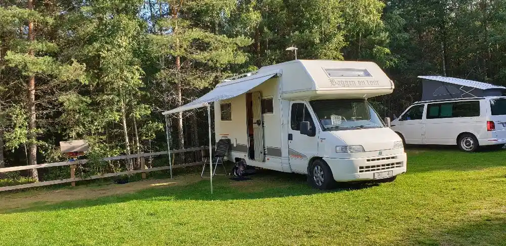 En husbil parkerad på Habo Camping och Stugby. Fordonet står på en grönskande gräsyta med träd och markeringar för campingplatser i bakgrunden.