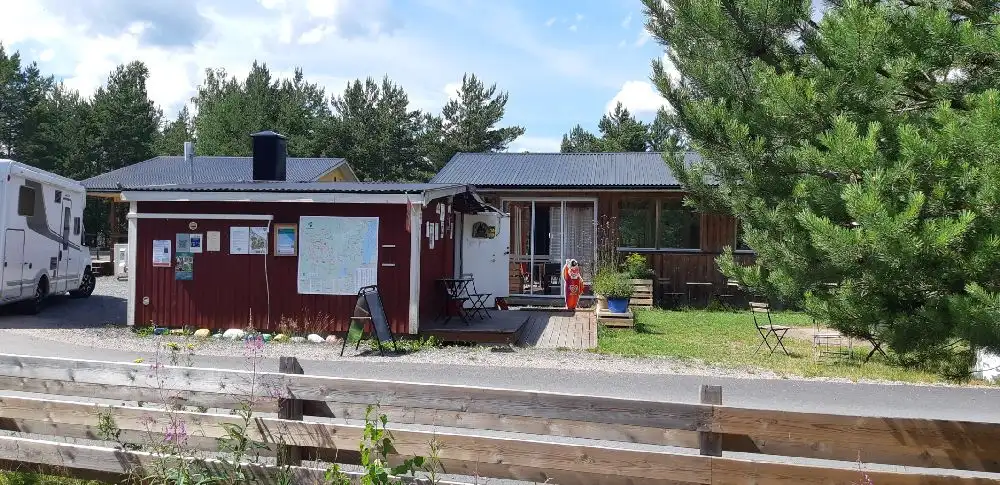 En lummig campingplats med husvagn och stugor omgivna av grönska. En uppfart och trädgårdsbyggnader syns i bakgrunden på Habo Camping och Stugby.