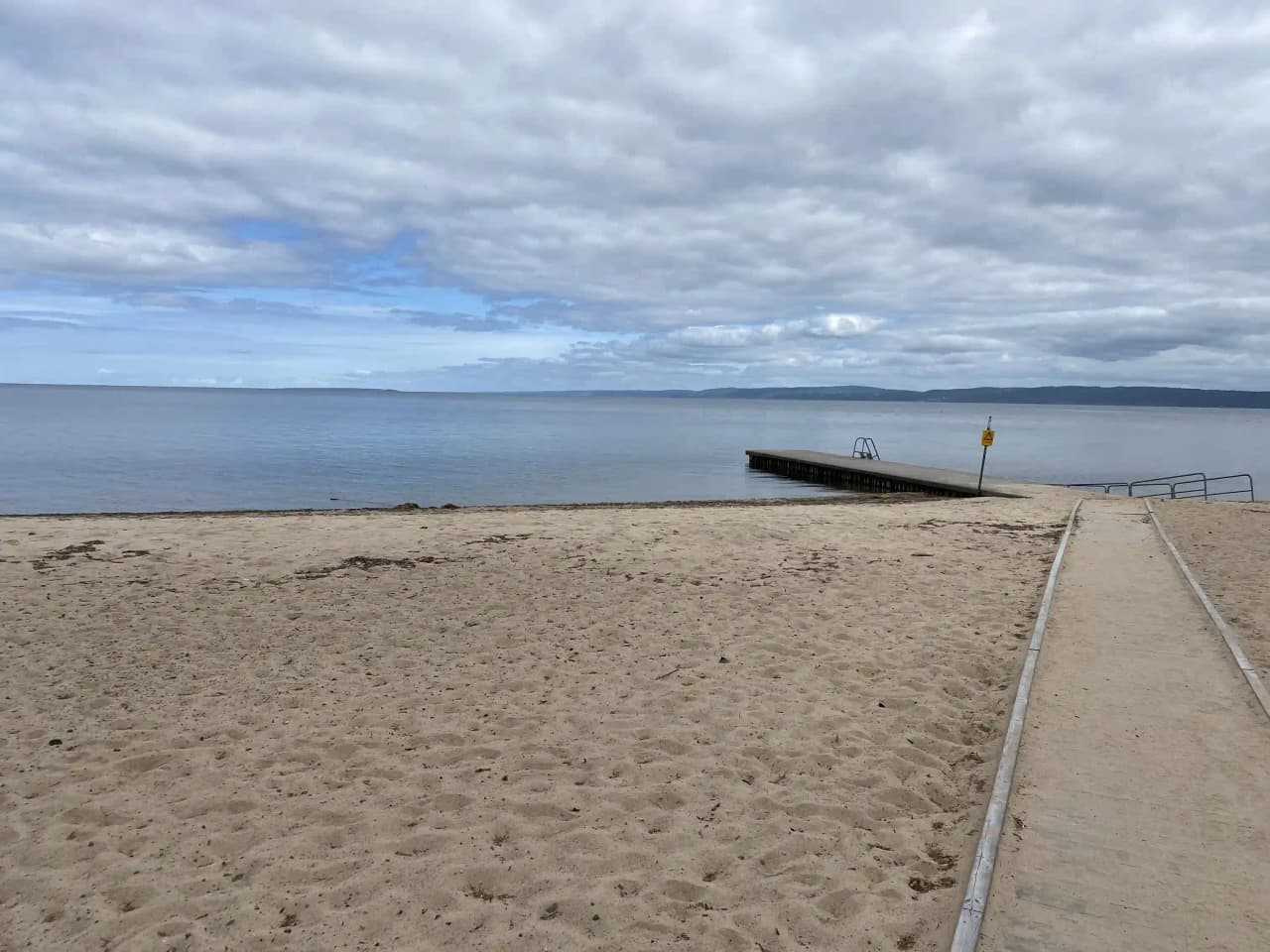 Strand med utsikt över havet och en vidsträckt horisont, omgiven av molnig himmel.
