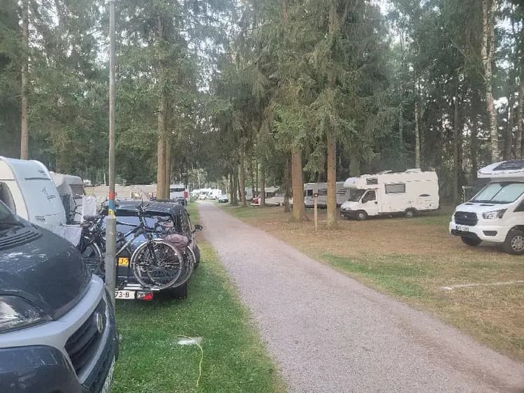 En campingplats med flera husvagnar och cyklar parkerade på grusig mark. Skog i bakgrunden.
