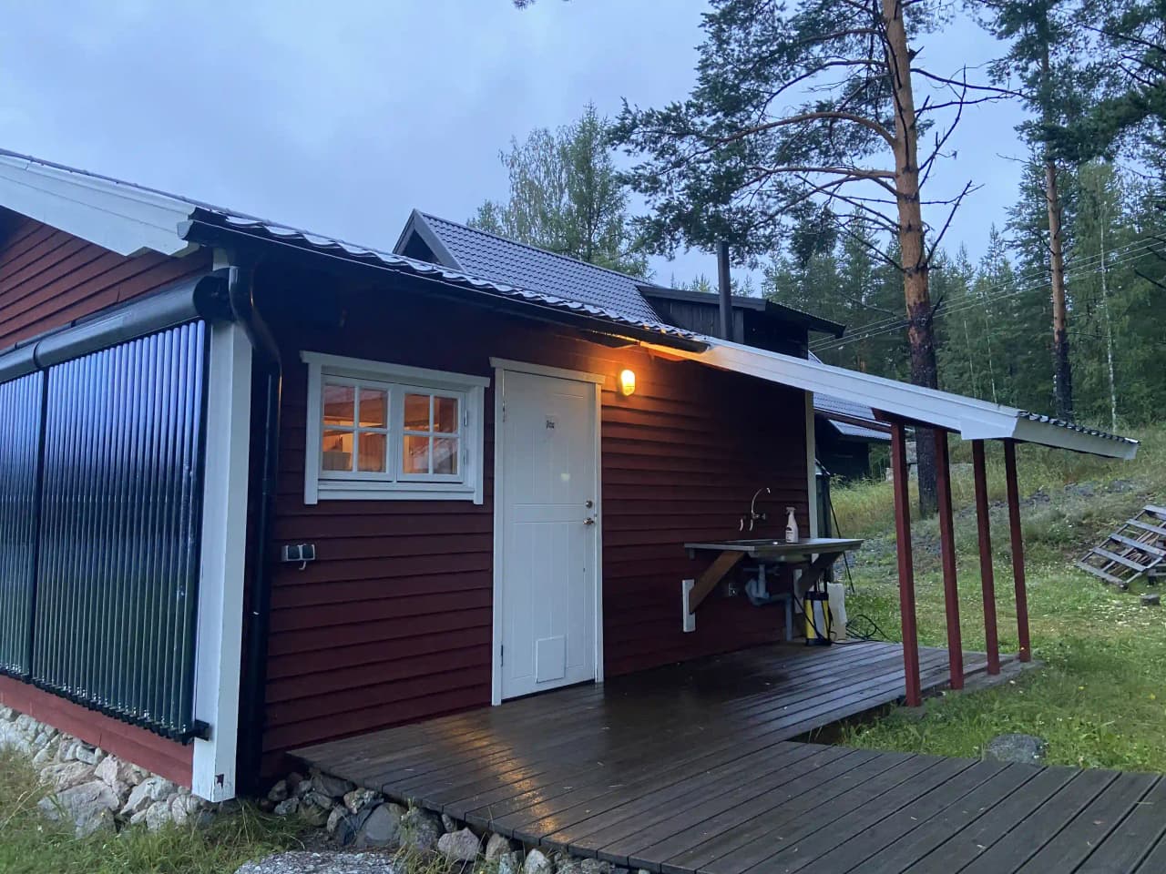 En röd trästuga med vita knutar och ett sadeltak, omgiven av en skogsmiljö. Byggnaden har en enkel dörr och är troligtvis en del av anläggningen Offroadsweden.