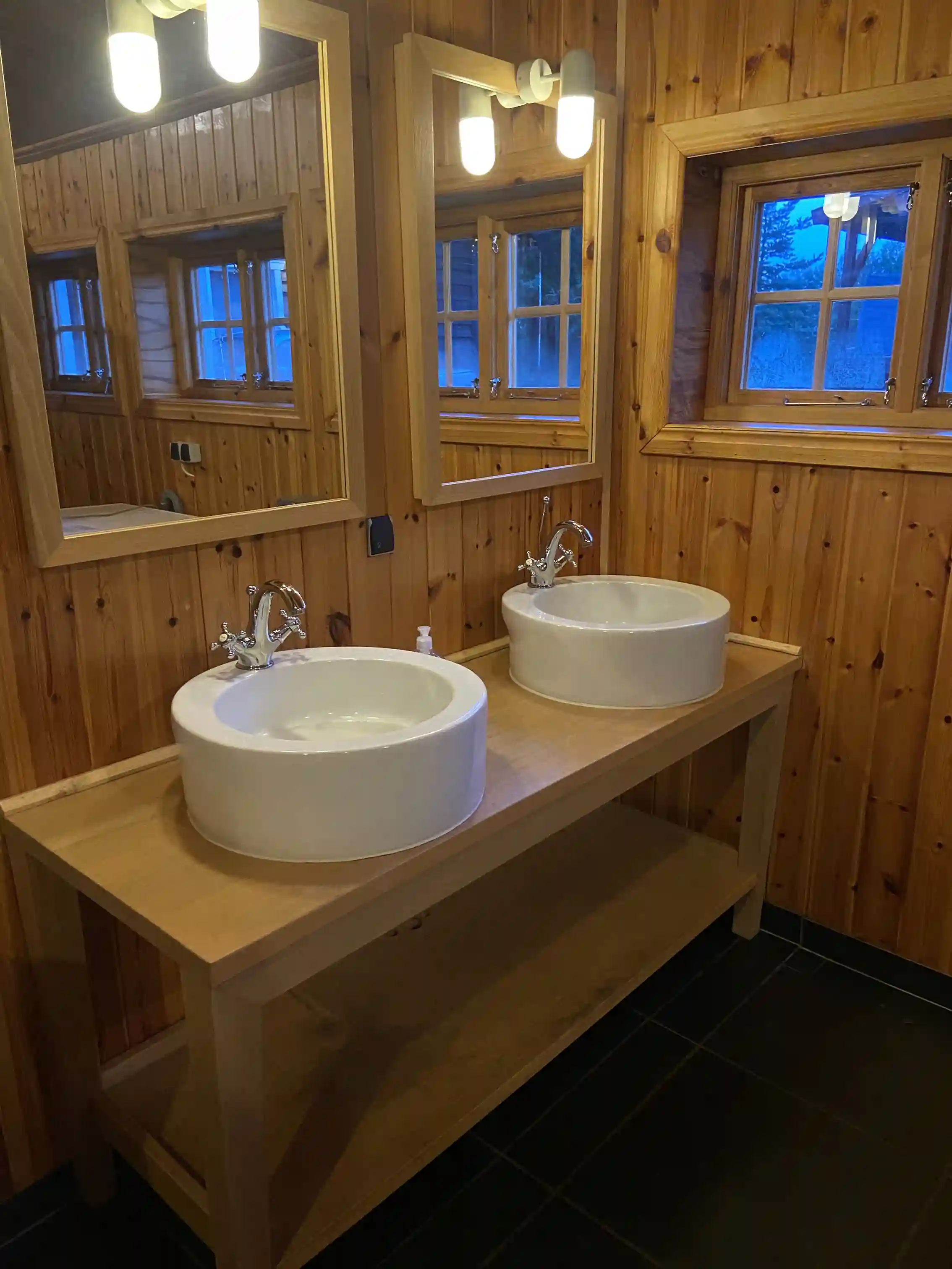 En inomhusmiljö med trädetaljer, golv och ett handfat med modern design, samt en kran installerad. Detaljer i trä skapar en varm och inbjudande atmosfär.