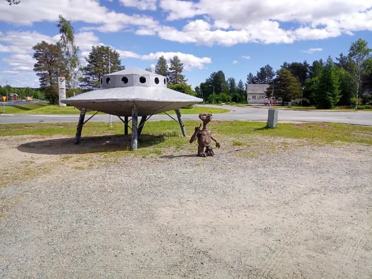 En campingplats med tallar i bakgrunden och en okänd flygande farkost synlig på himlen.