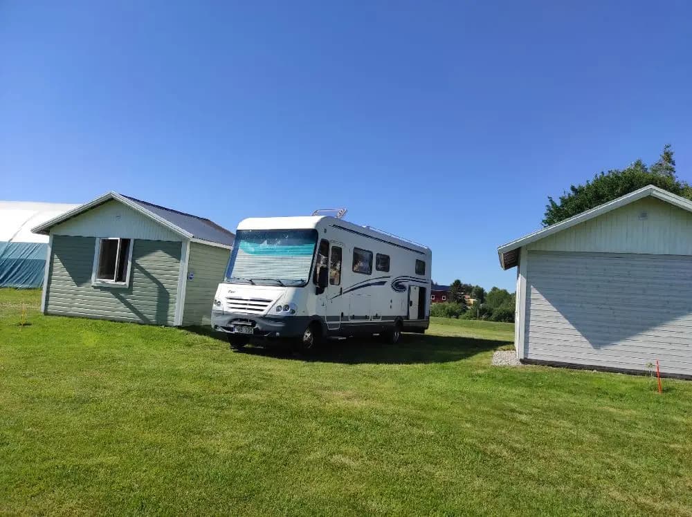 Bild av Sangis Motell och Camping med husvagnar och tält uppställda på en grön gräsmatta. Olika rekreationsfordon syns parkerade i området, blandat med mobila hem och ett semi-trailer lastfordon. En lugn campingmiljö i en park-liknande omgivning.