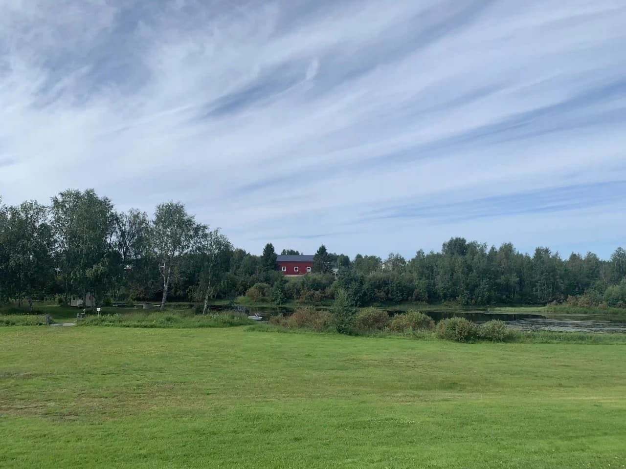 En grönskande campingplats och motell i Sangis med öppet gräslandskap, omgivna av träd under en klar dag med blå himmel.